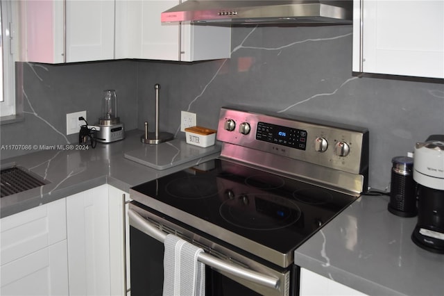 kitchen featuring electric range, wall chimney exhaust hood, white cabinets, and backsplash