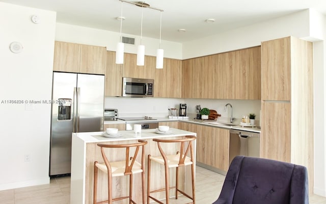 kitchen with a breakfast bar, stainless steel appliances, sink, light brown cabinets, and a kitchen island