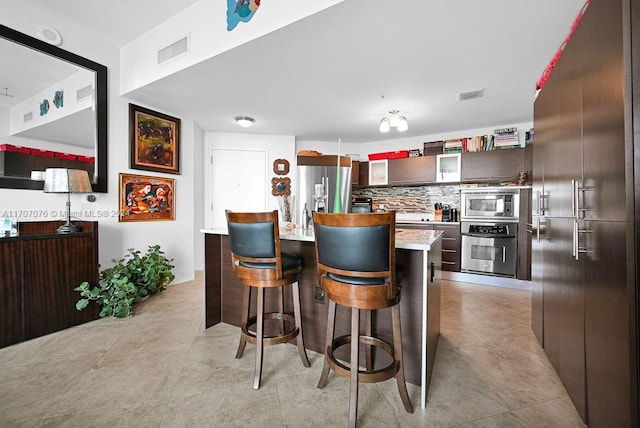 kitchen with decorative backsplash, appliances with stainless steel finishes, a breakfast bar, dark brown cabinetry, and a kitchen island