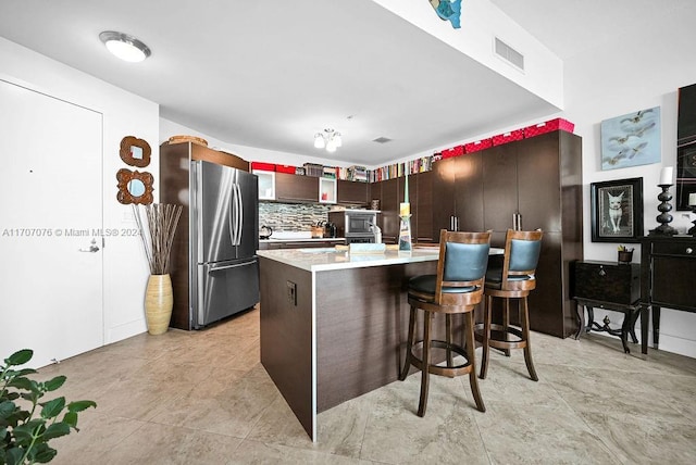 kitchen featuring appliances with stainless steel finishes, dark brown cabinets, a breakfast bar, and tasteful backsplash