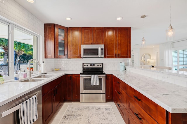 kitchen featuring sink, hanging light fixtures, light stone countertops, appliances with stainless steel finishes, and plenty of natural light