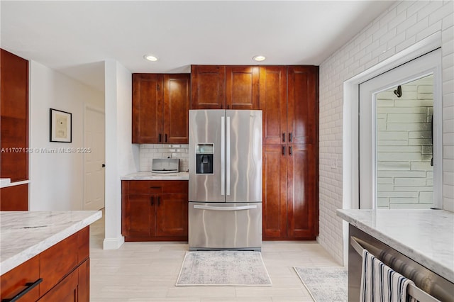 kitchen featuring light stone counters, backsplash, and stainless steel fridge