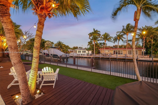 deck at dusk with a water view and a lawn