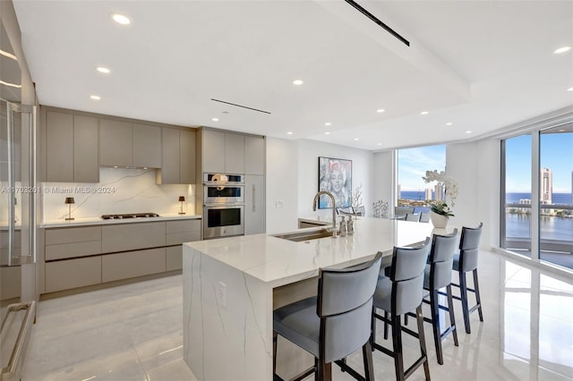 kitchen with gray cabinetry, sink, stainless steel double oven, a large island with sink, and a water view