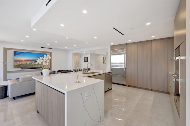 kitchen featuring gray cabinetry, dishwasher, a large island with sink, sink, and light stone counters