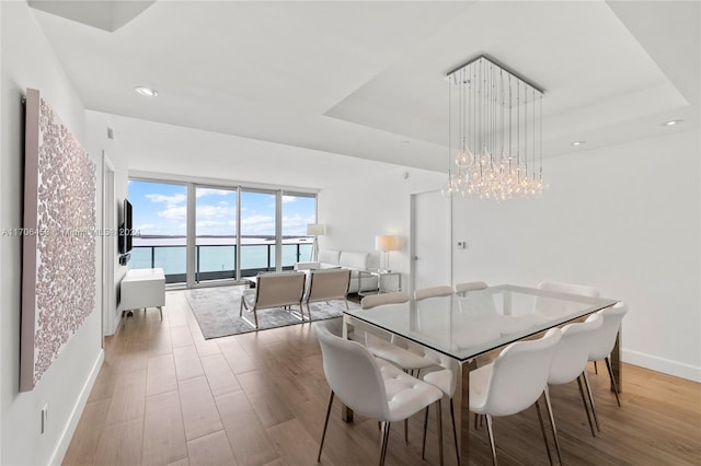 dining area featuring an inviting chandelier, light hardwood / wood-style floors, and a raised ceiling