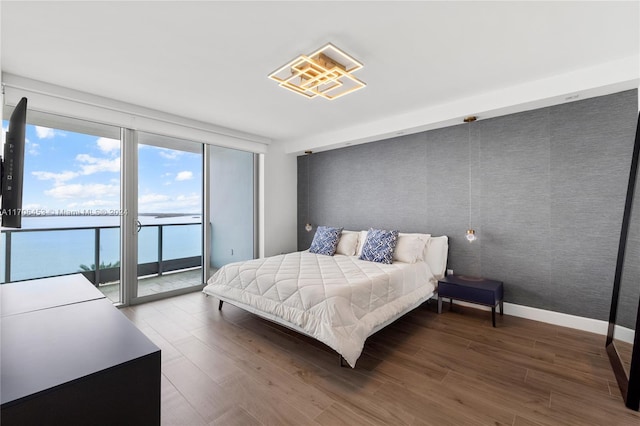 bedroom featuring access to outside, hardwood / wood-style floors, and a water view