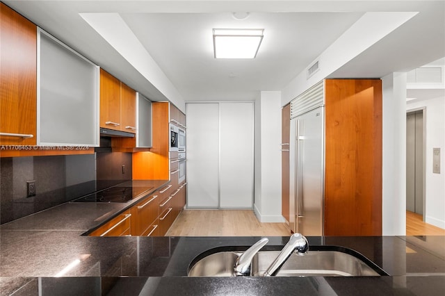 kitchen with built in appliances, light hardwood / wood-style floors, and sink