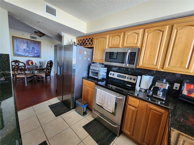 kitchen with a textured ceiling, stainless steel appliances, light hardwood / wood-style flooring, and dark stone countertops