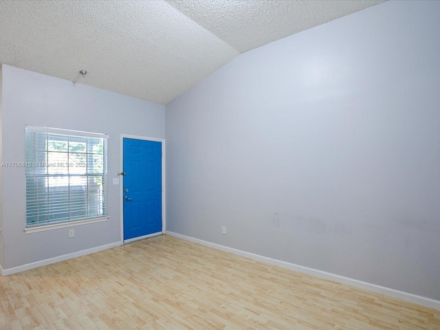 empty room featuring a textured ceiling, light wood-type flooring, and vaulted ceiling