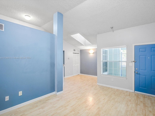 foyer with a textured ceiling, light hardwood / wood-style floors, and vaulted ceiling with skylight