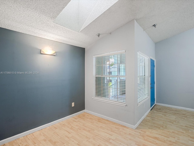 spare room with light wood-type flooring, a textured ceiling, and vaulted ceiling with skylight