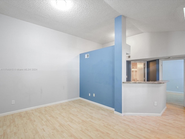 spare room featuring lofted ceiling, a textured ceiling, and light wood-type flooring