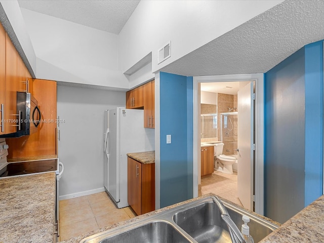 kitchen with a textured ceiling, sink, white refrigerator with ice dispenser, light tile patterned floors, and range