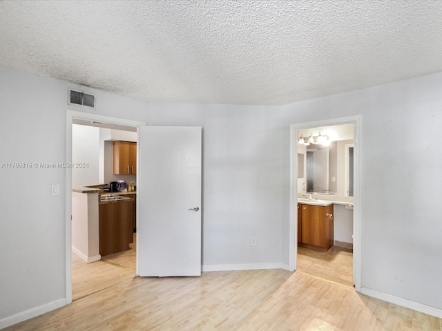 unfurnished bedroom featuring connected bathroom, sink, light hardwood / wood-style floors, and a textured ceiling