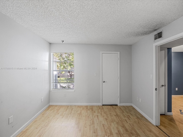 spare room with a textured ceiling and light hardwood / wood-style flooring