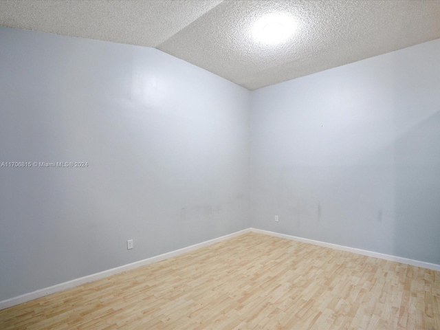 spare room featuring a textured ceiling, light hardwood / wood-style flooring, and lofted ceiling