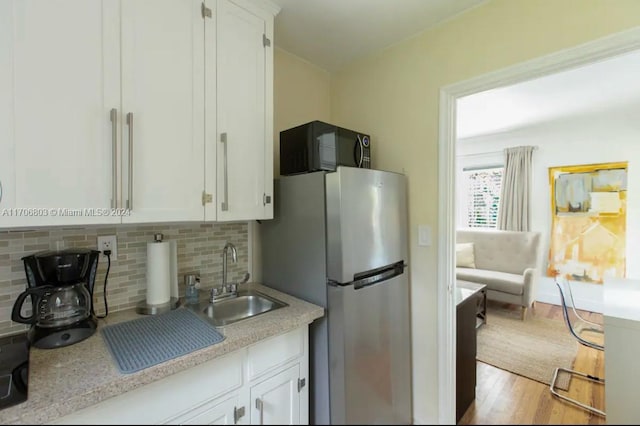 kitchen with decorative backsplash, stainless steel fridge, light wood-type flooring, sink, and white cabinets