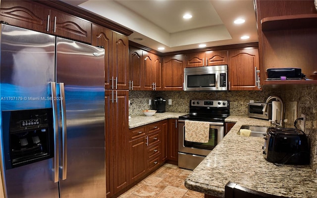 kitchen with appliances with stainless steel finishes, backsplash, light stone counters, a tray ceiling, and sink