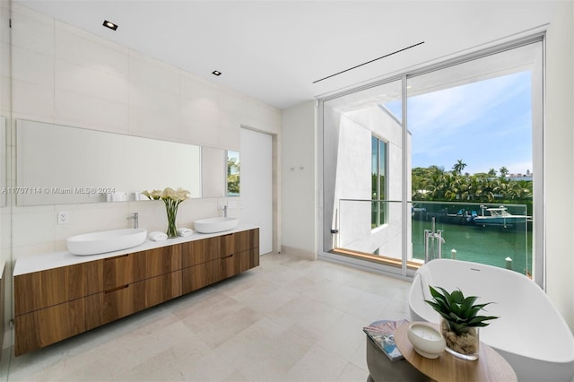 bathroom featuring vanity, a water view, a tub to relax in, and tile walls