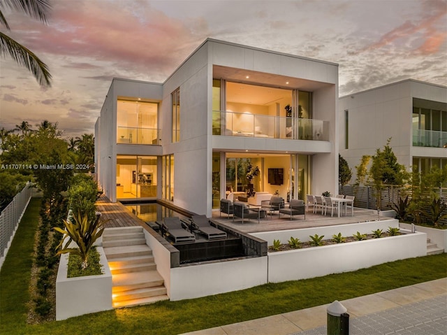 back house at dusk with an outdoor hangout area, a balcony, and a patio area