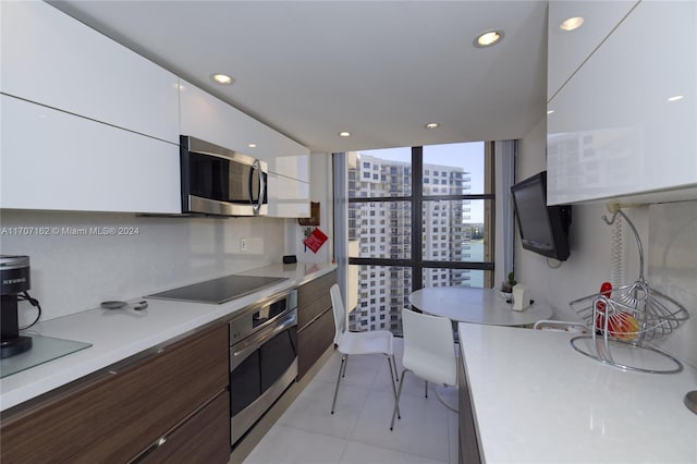 kitchen with floor to ceiling windows, white cabinetry, dark brown cabinetry, light tile patterned floors, and appliances with stainless steel finishes