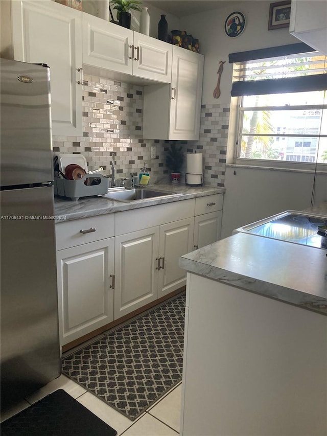 kitchen featuring sink, decorative backsplash, light tile patterned floors, white cabinetry, and stainless steel refrigerator