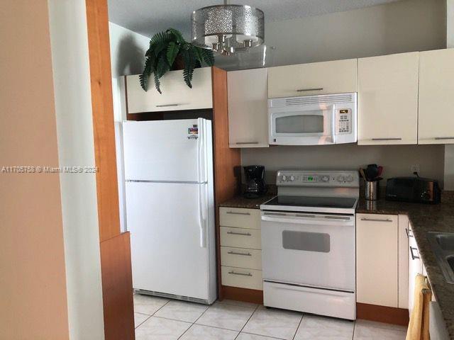 kitchen featuring white appliances, a textured ceiling, light tile patterned floors, a chandelier, and white cabinetry