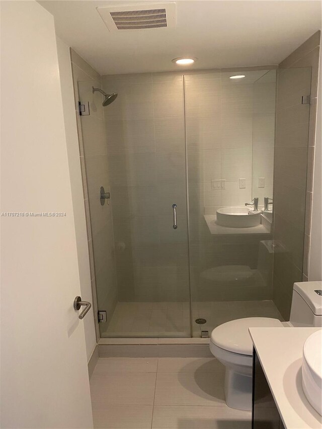 bathroom with toilet, vanity, tile patterned floors, and a shower with door