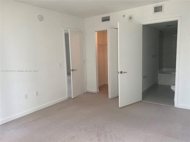 unfurnished bedroom featuring light carpet, connected bathroom, a spacious closet, and a closet