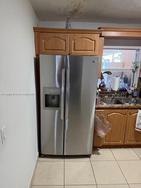 kitchen featuring dark stone countertops, stainless steel fridge with ice dispenser, sink, and light tile patterned floors