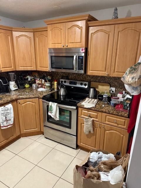 kitchen featuring tasteful backsplash, light tile patterned floors, dark stone counters, and appliances with stainless steel finishes