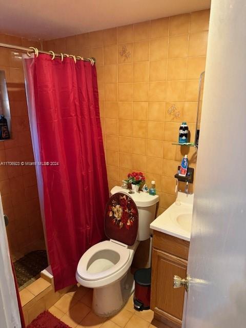 bathroom featuring curtained shower, tile patterned flooring, toilet, vanity, and tile walls