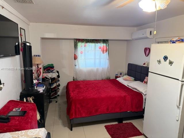 tiled bedroom with white fridge, an AC wall unit, and ceiling fan