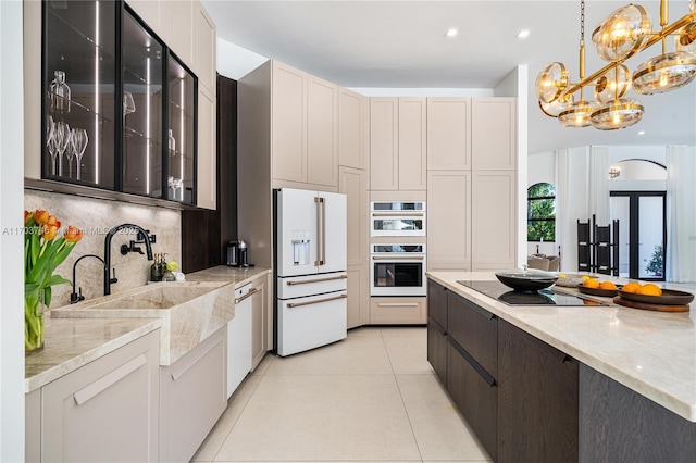 kitchen with light tile patterned floors, a notable chandelier, white appliances, dark brown cabinets, and light stone counters