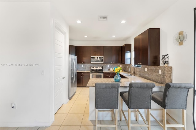 kitchen featuring sink, kitchen peninsula, a breakfast bar, dark brown cabinets, and appliances with stainless steel finishes