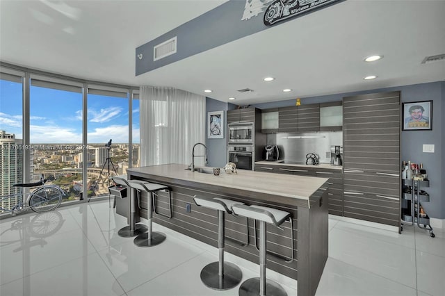 kitchen featuring appliances with stainless steel finishes, a kitchen island with sink, sink, light tile patterned floors, and a wall of windows