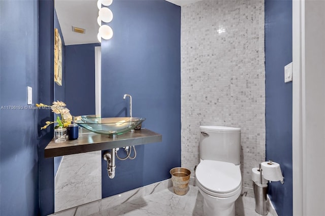 bathroom featuring toilet, sink, and tile walls