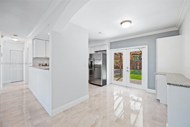 kitchen with white cabinetry, french doors, light stone counters, stainless steel fridge, and ornamental molding