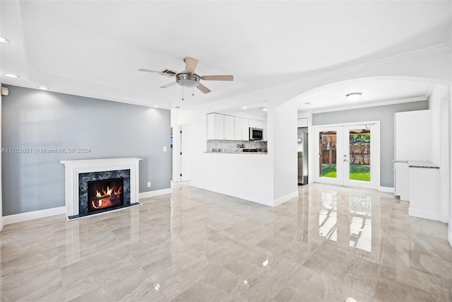 unfurnished living room featuring ceiling fan, french doors, a high end fireplace, and ornamental molding