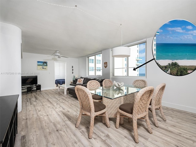 dining area with light wood-type flooring, ceiling fan, and a water view