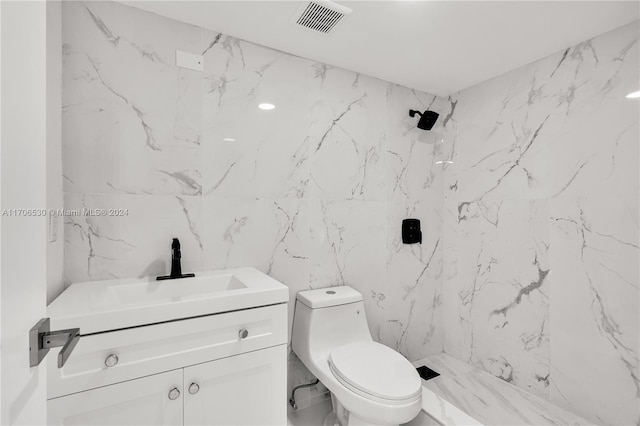 bathroom with a tile shower, vanity, toilet, and tile walls