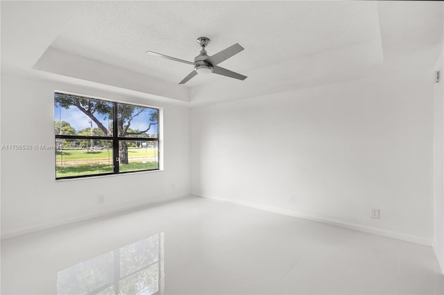 unfurnished room with a raised ceiling, ceiling fan, and a textured ceiling