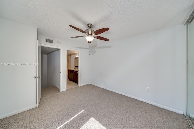 unfurnished bedroom featuring ceiling fan, ensuite bathroom, light carpet, and a textured ceiling