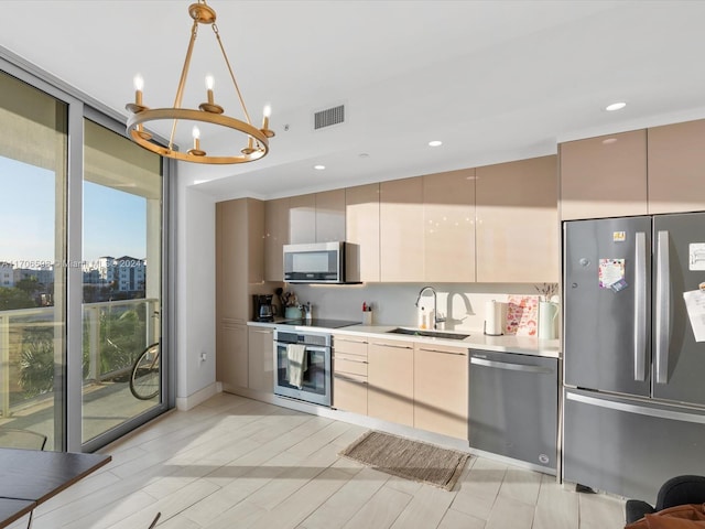 kitchen with pendant lighting, an inviting chandelier, sink, light wood-type flooring, and appliances with stainless steel finishes