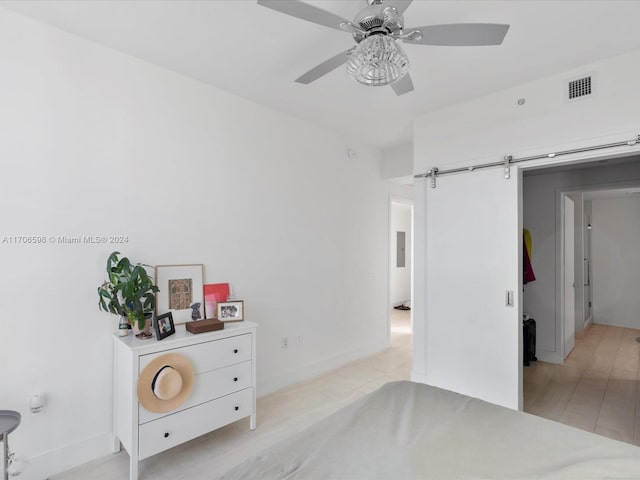 bedroom featuring ceiling fan, a barn door, and light wood-type flooring