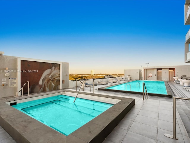 pool at dusk featuring a hot tub