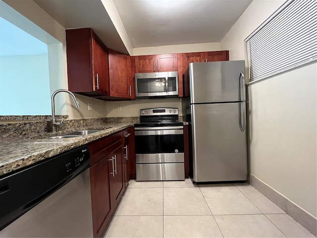 kitchen with sink, light tile patterned floors, stainless steel appliances, and dark stone counters