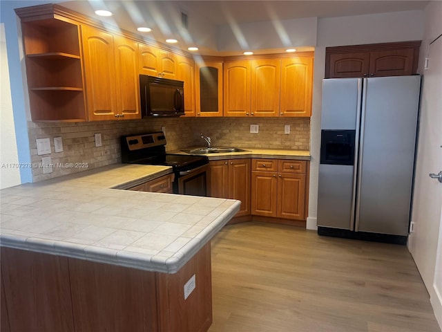 kitchen with a peninsula, light wood-style flooring, a sink, glass insert cabinets, and appliances with stainless steel finishes