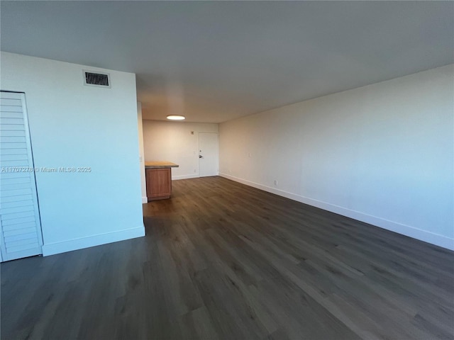 empty room featuring baseboards, dark wood-type flooring, and visible vents
